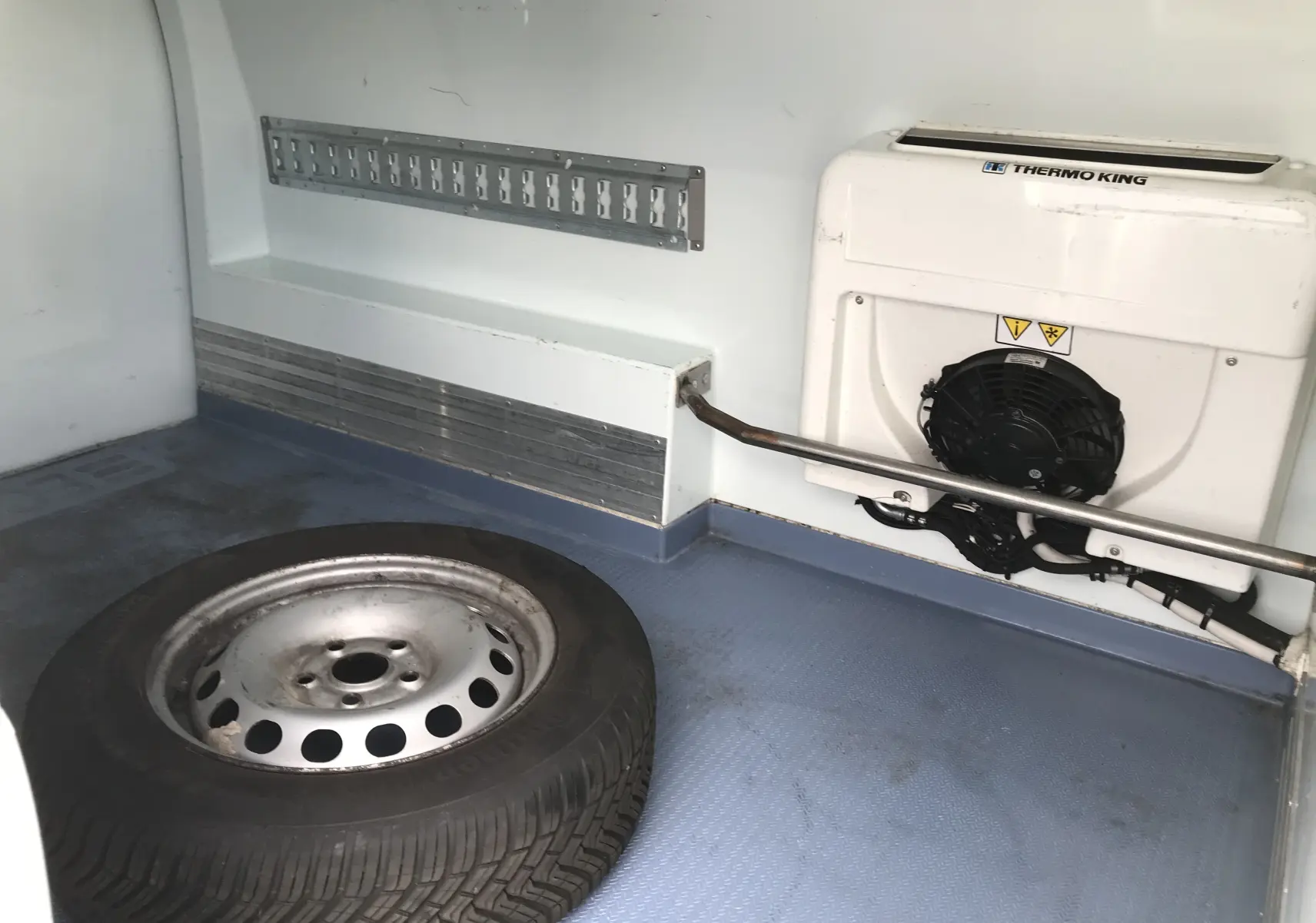 Vue intérieure du compartiment frigorifique blanc du Volkswagen Caddy Maxi Van 2015, avec roue de secours et unité Thermo King.