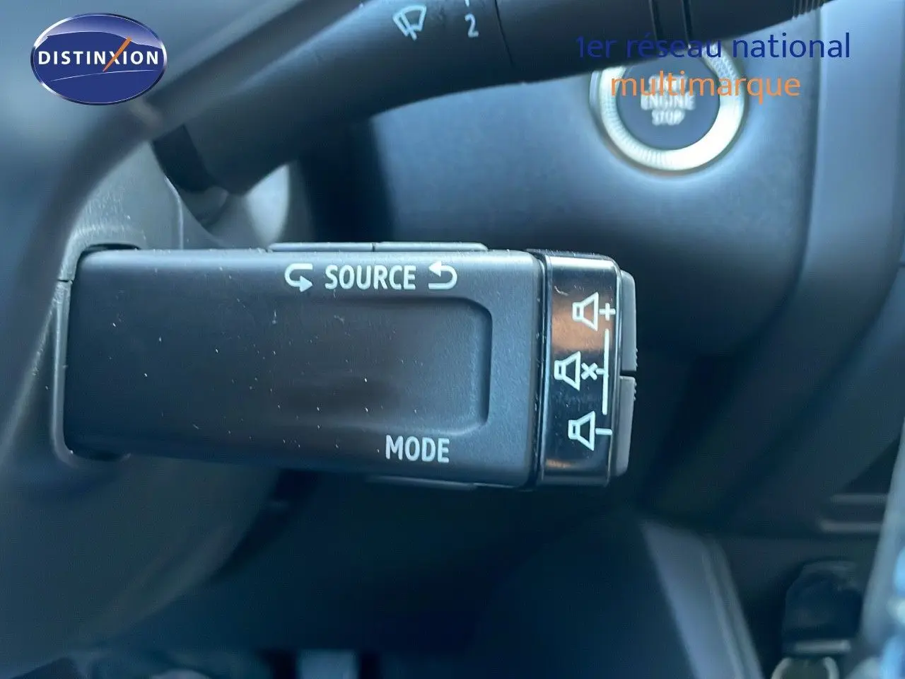 Gros plan sur la commande au volant du Renault Captur E-Tech blanc nacré avec bouton source et mode, intérieur noir.