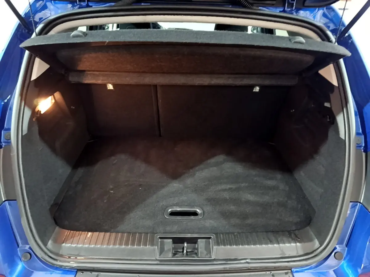Coffre ouvert vu de l'arrière d'un Renault Captur bleu 2023, avec plancher plat et éclairage intérieur à gauche.