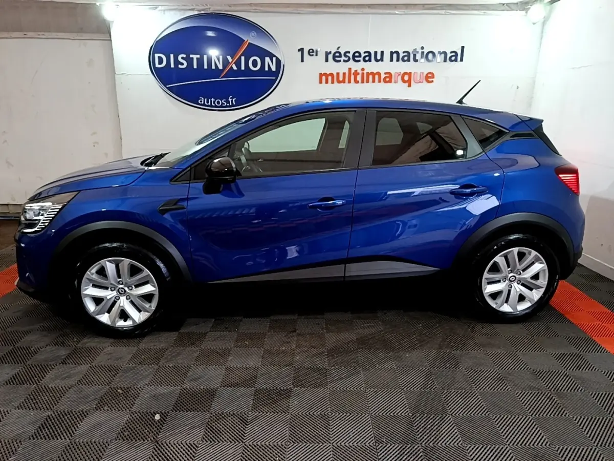 Vue de profil côté gauche d'un Renault Captur bleu 2023 avec jantes argentées, dans un showroom intérieur.