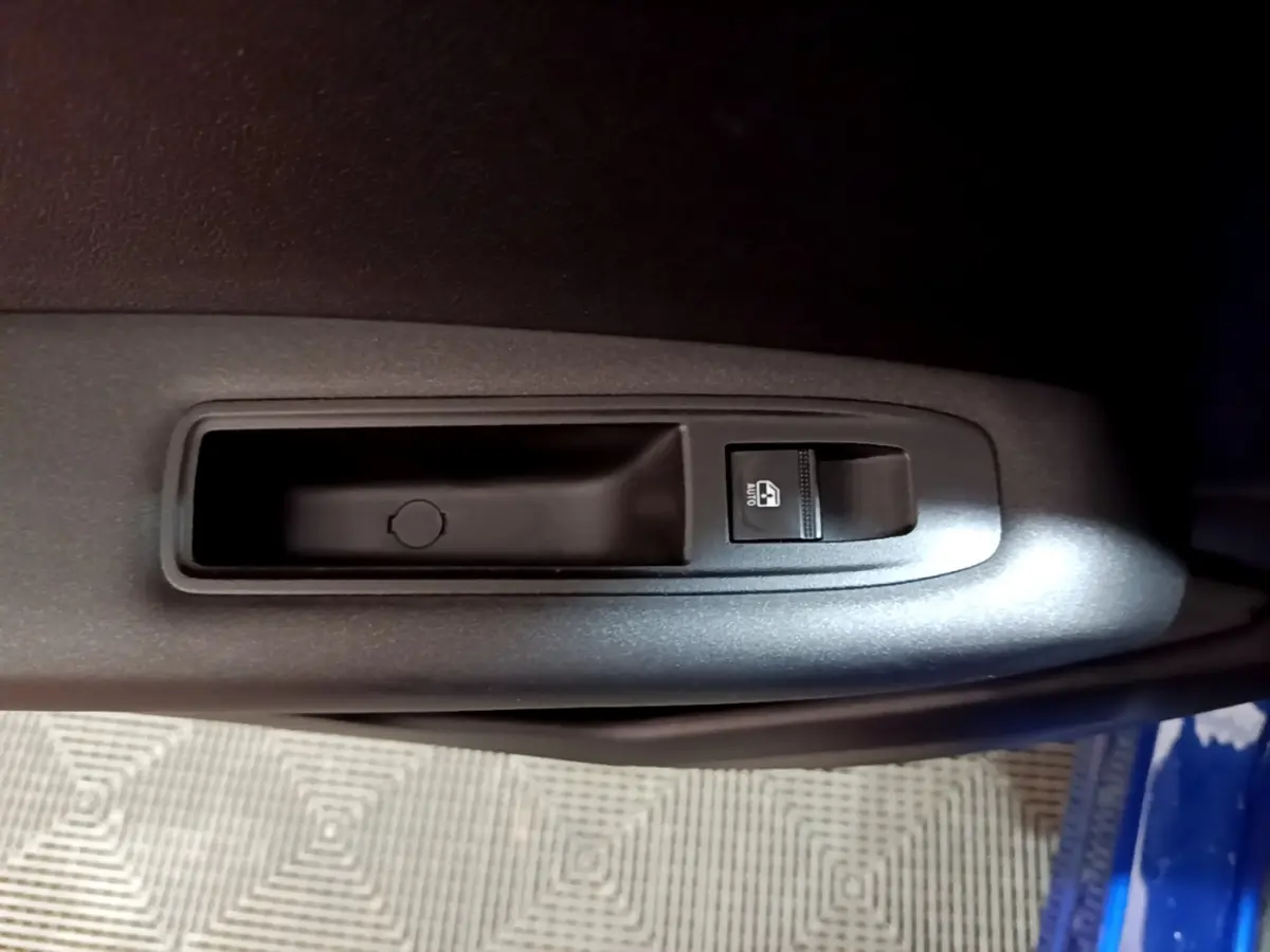 Gros plan sur le bouton de commande de la vitre électrique côté conducteur d’un Renault Captur bleu 2023.