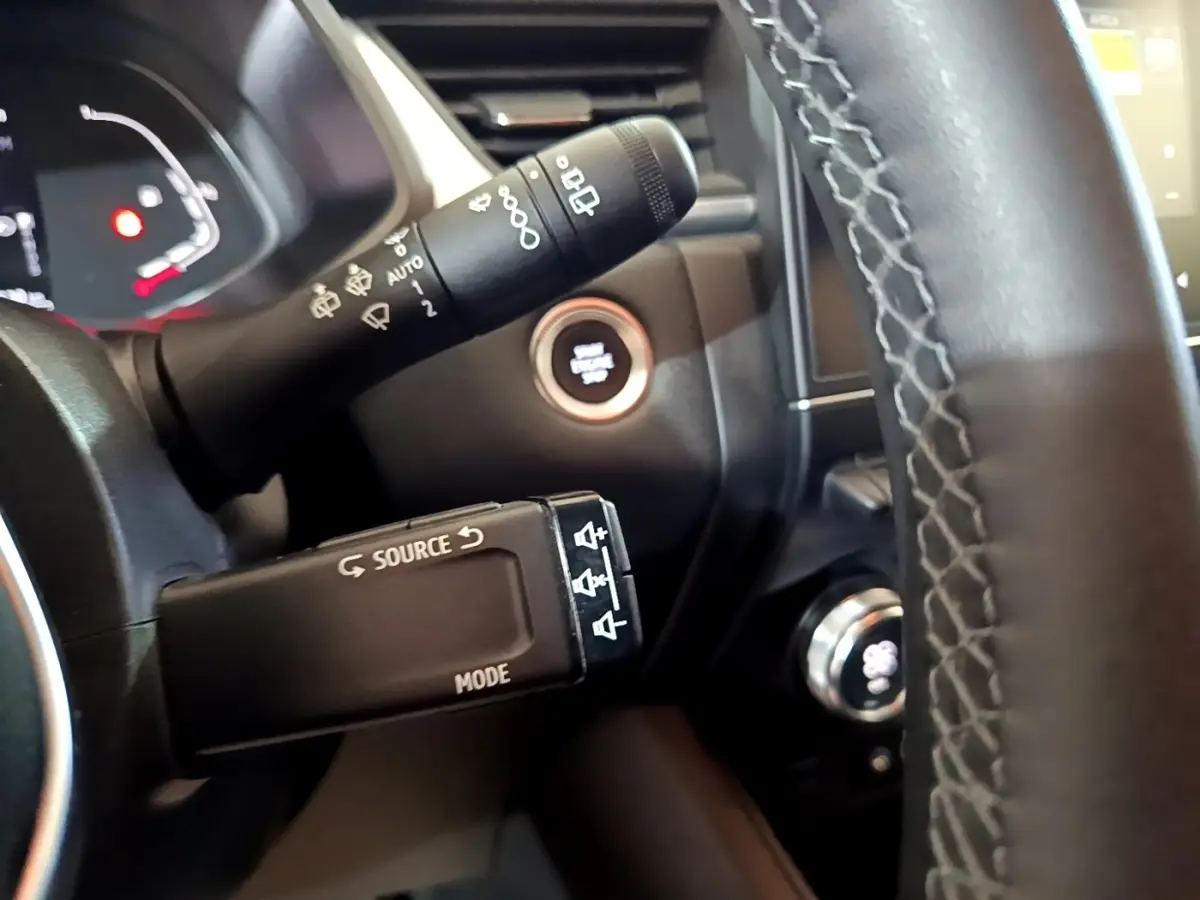 Gros plan intérieur sur le volant noir et les commandes de Renault Captur bleu, avec bouton démarrage et tableau de bord partiel.