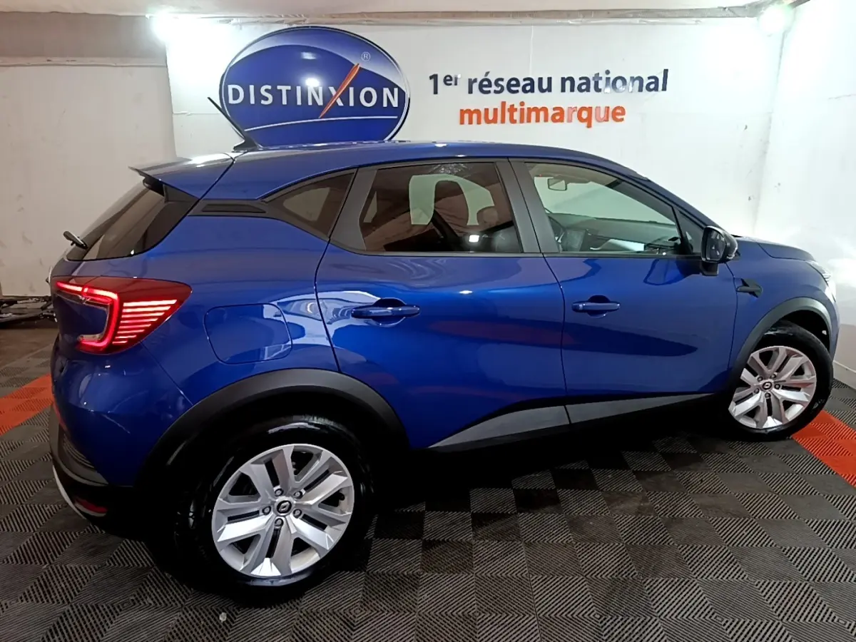 Vue côté droit du Renault Captur bleu 2023 en version hybride, avec feux arrière LED allumés dans un showroom.