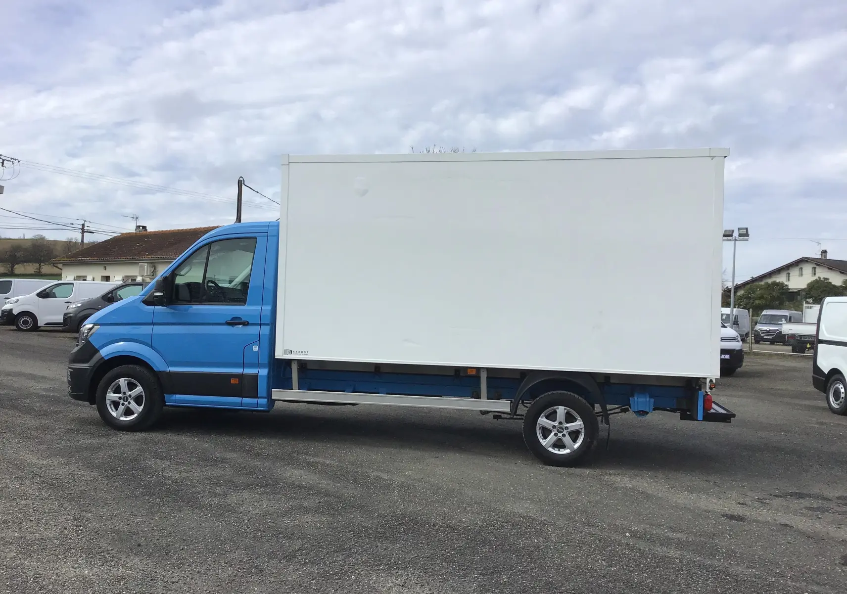 Vue de profil côté gauche d'un Volkswagen Crafter bleu avec caisse blanche de grande capacité sur un parking.