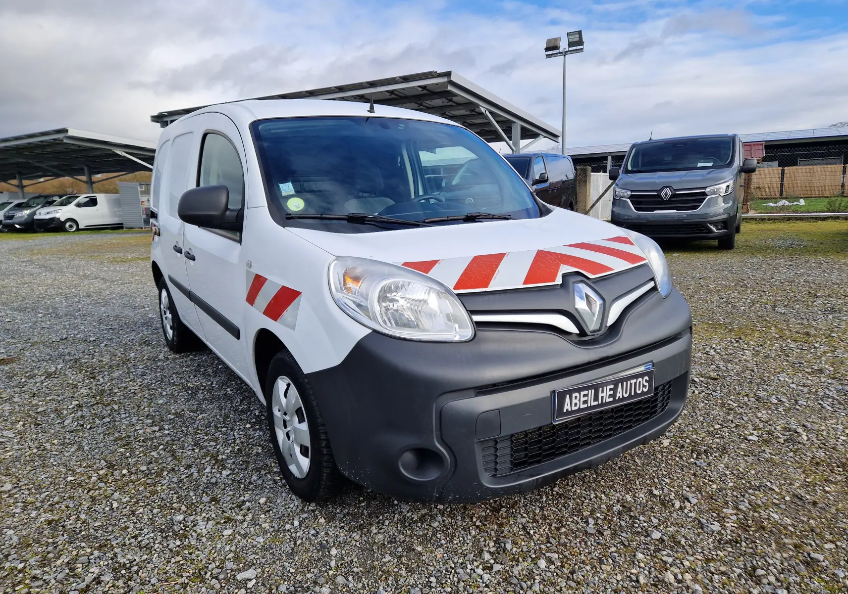 Vue 3/4 avant gauche d’un Renault Kangoo blanc 2020 avec bandes rouges diagonales sur capot et porte avant.