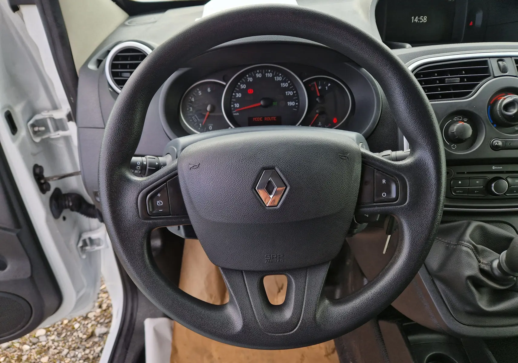 Vue intérieure centrée sur le volant noir d’un Renault Kangoo blanc 2020 avec tableau de bord et levier de vitesses manuel visibles.