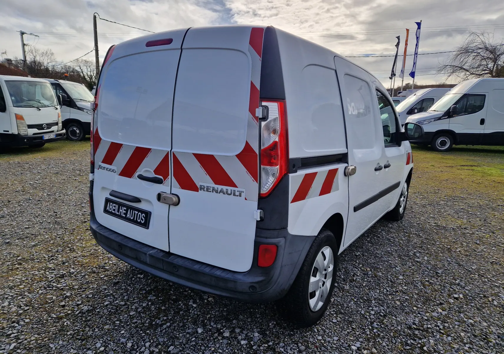 Vue 3/4 arrière droite d’un Renault Kangoo blanc 2020 avec bandes rouges réfléchissantes et plaque Abeilhe Autos.