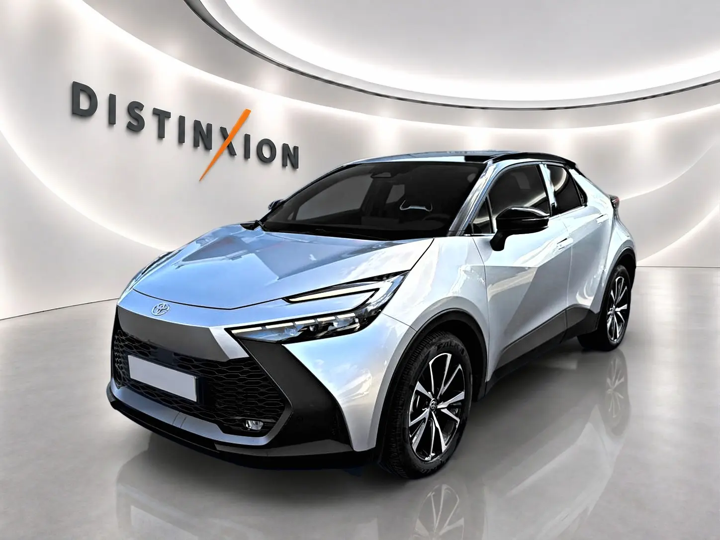 Toyota C-HR gris 3/4 avant droit avec toit noir et jantes alliage dans un showroom lumineux.