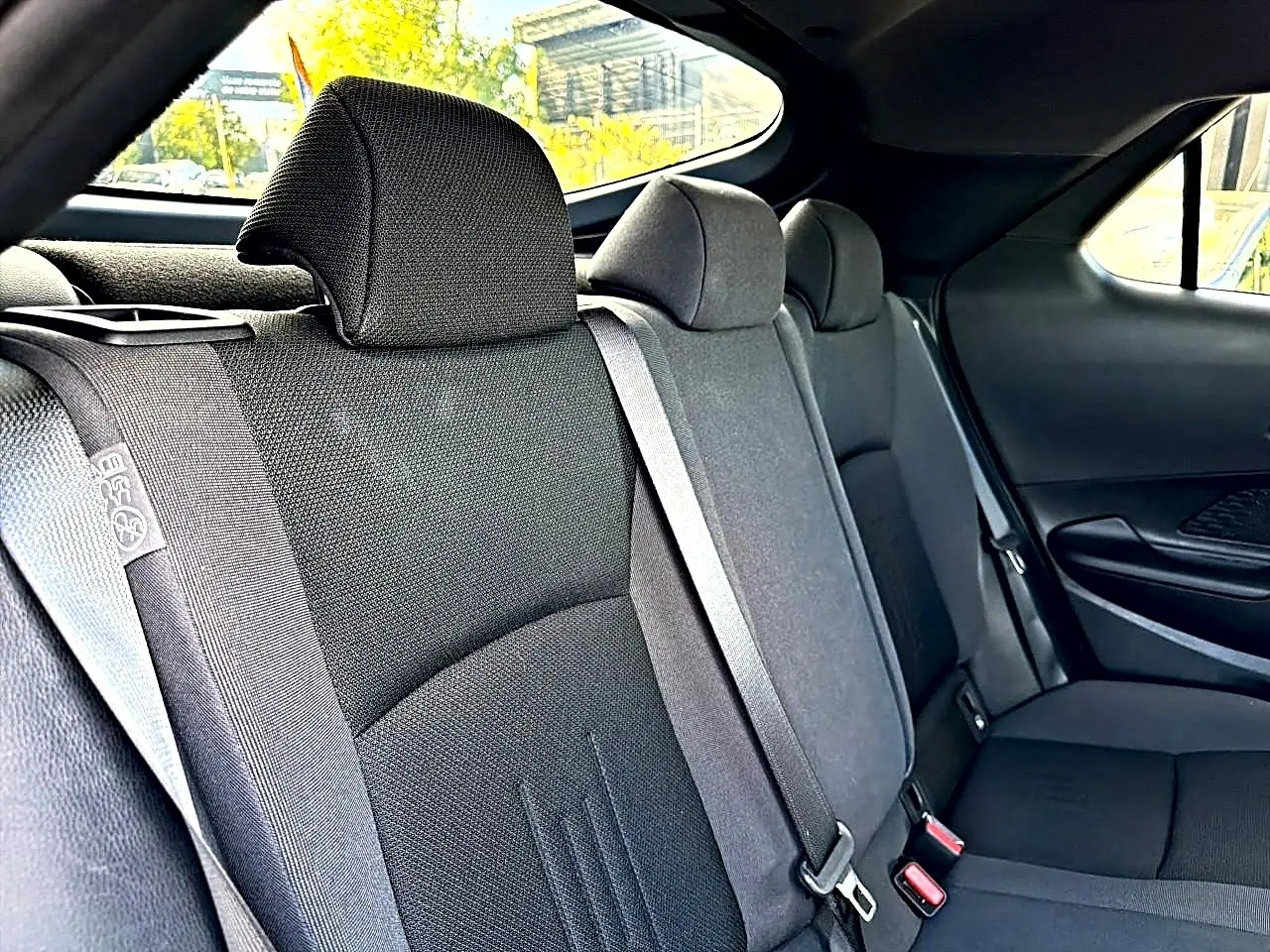 Vue intérieure arrière du Toyota C-HR 1.8 hybride 2025, montrant les sièges tissu gris foncé et les ceintures de sécurité.