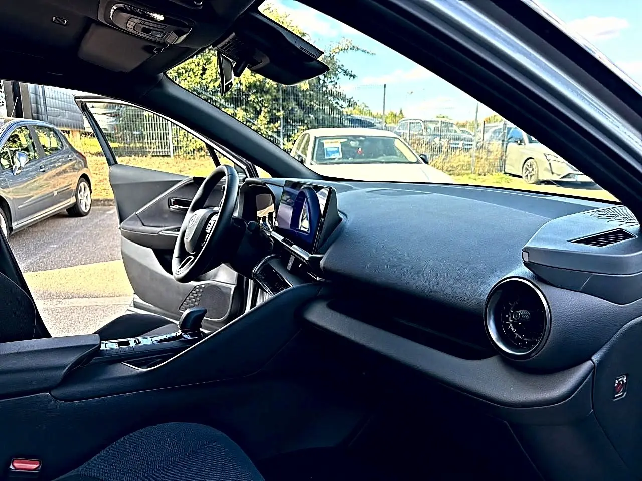 Intérieur du Toyota C-HR 1.8 hybride 2025 vu côté conducteur, tableau de bord noir avec écran tactile central.