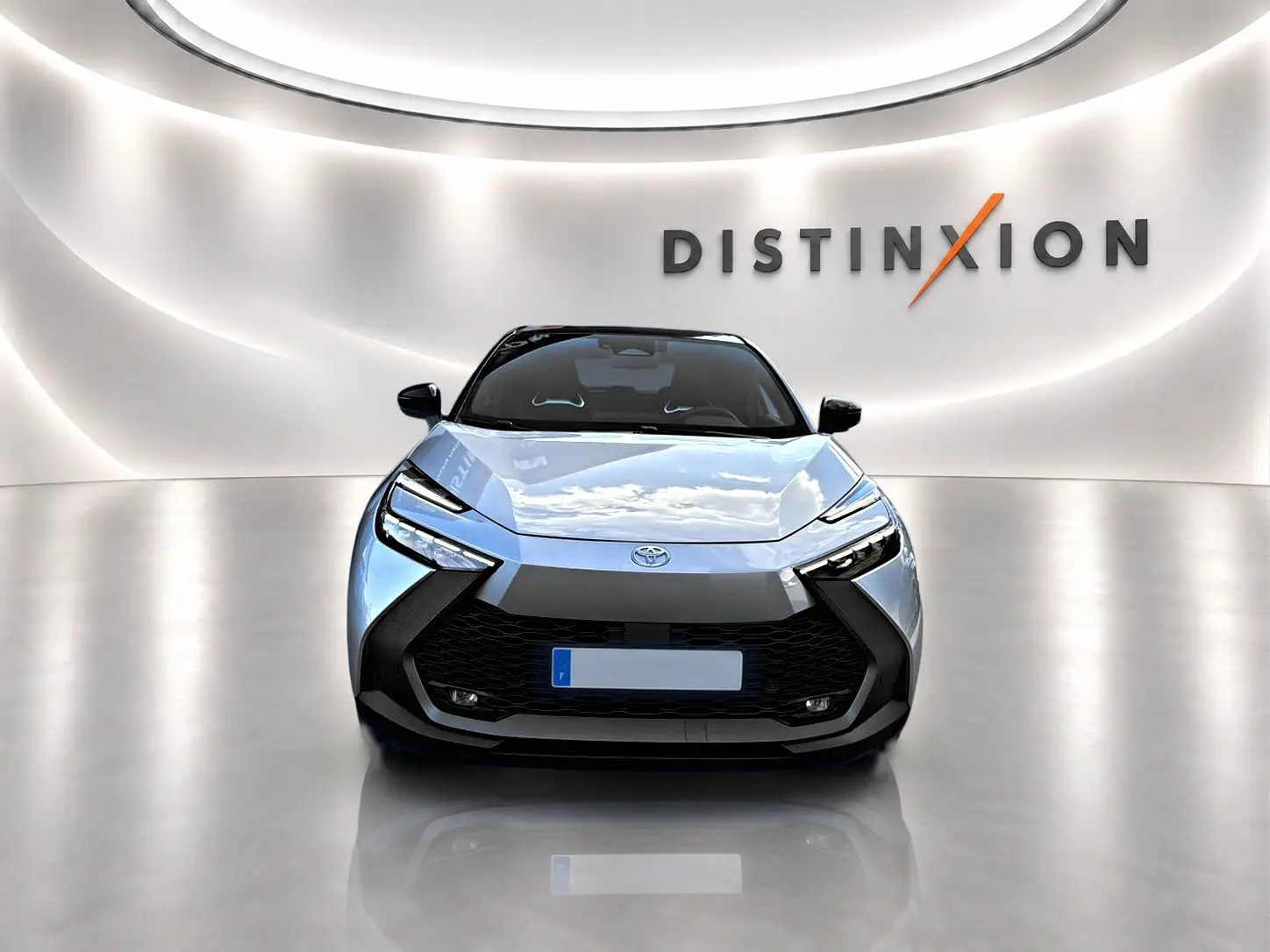 Vue avant d'un Toyota C-HR gris 2025 avec calandre noire et phares LED, dans un showroom lumineux "Distinxion".