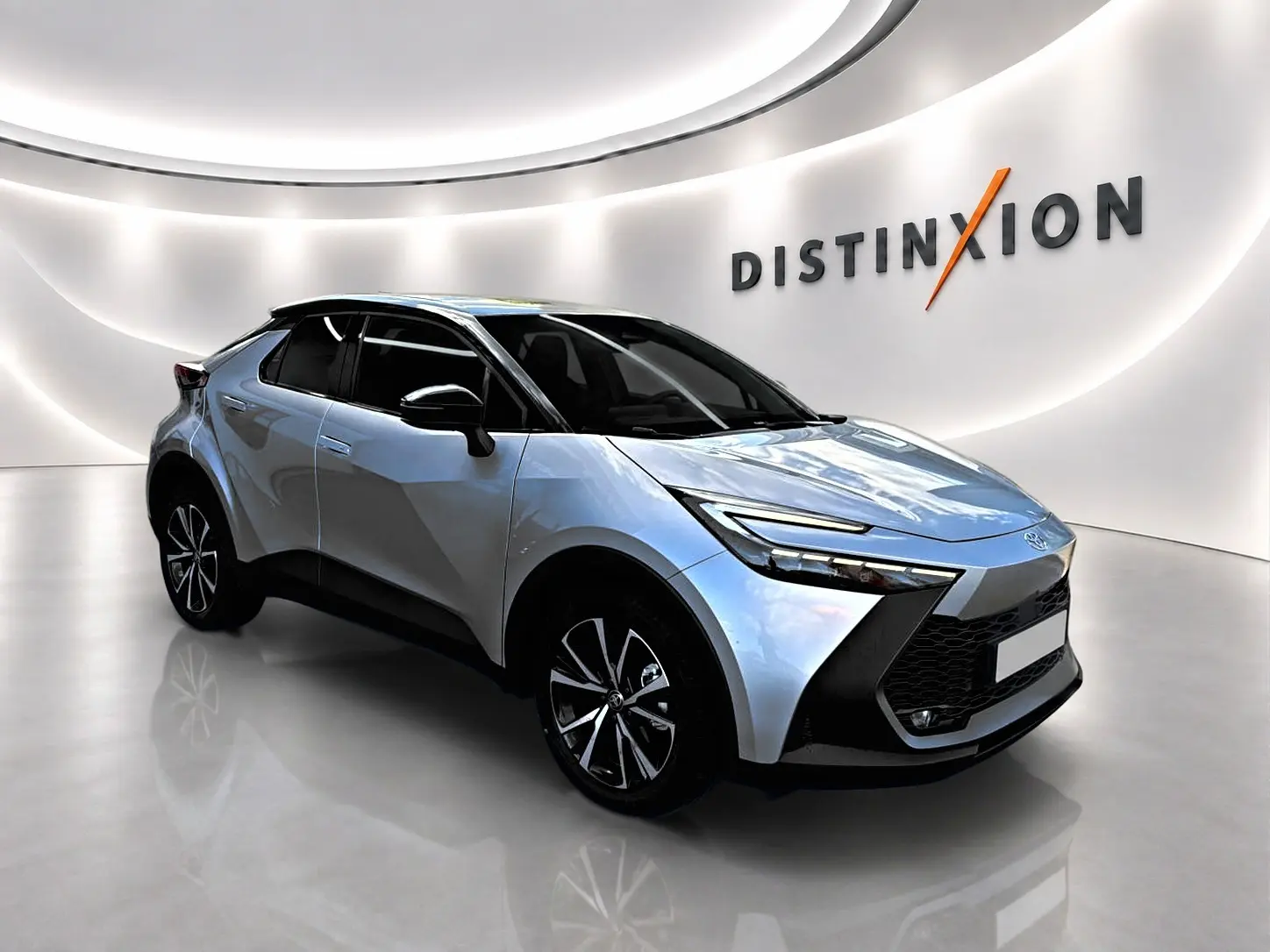 Toyota C-HR 1.8 hybride gris en 3/4 avant droit, avec jantes alliage et toit noir brillant dans un showroom lumineux.