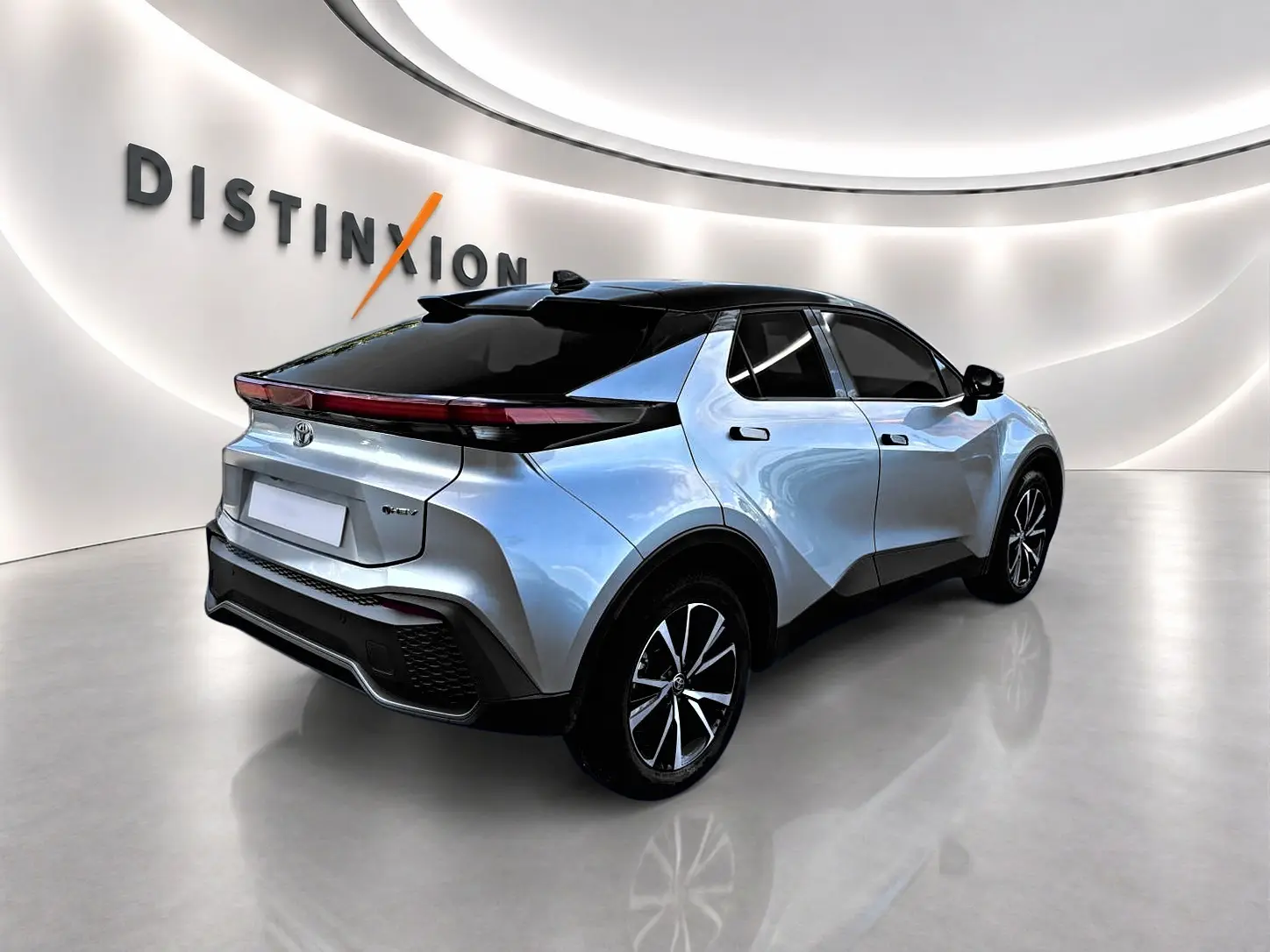 Toyota C-HR hybride gris 3/4 arrière droit, toit noir et jantes alliage dans un showroom lumineux.