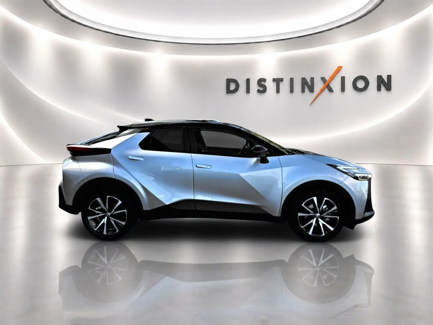 Vue de profil côté gauche du Toyota C-HR 1.8 hybride gris clair avec toit noir dans un showroom lumineux.