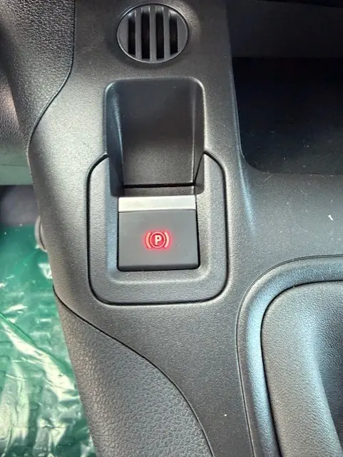 Gros plan sur le bouton de frein à main électrique rouge dans l'habitacle noir du Citroën Berlingo blanc 2026.