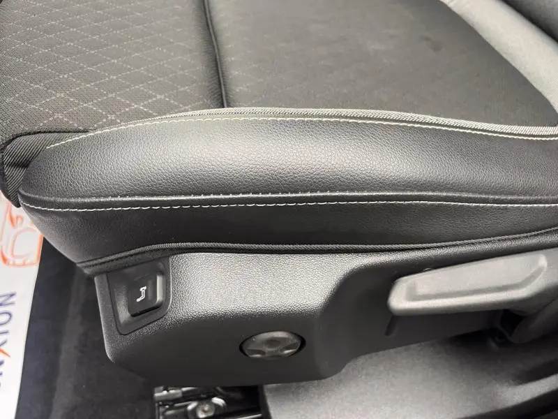 Détail de l'accoudoir et réglage électrique du siège conducteur en tissu noir avec surpiqûres blanches dans un Opel Grandland gris.