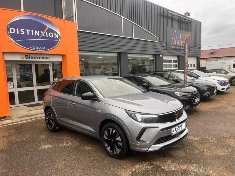 Vue 3/4 avant gauche d'un Opel Grandland gris Kontrast métallisé avec jantes bi-ton 18 pouces devant un garage.