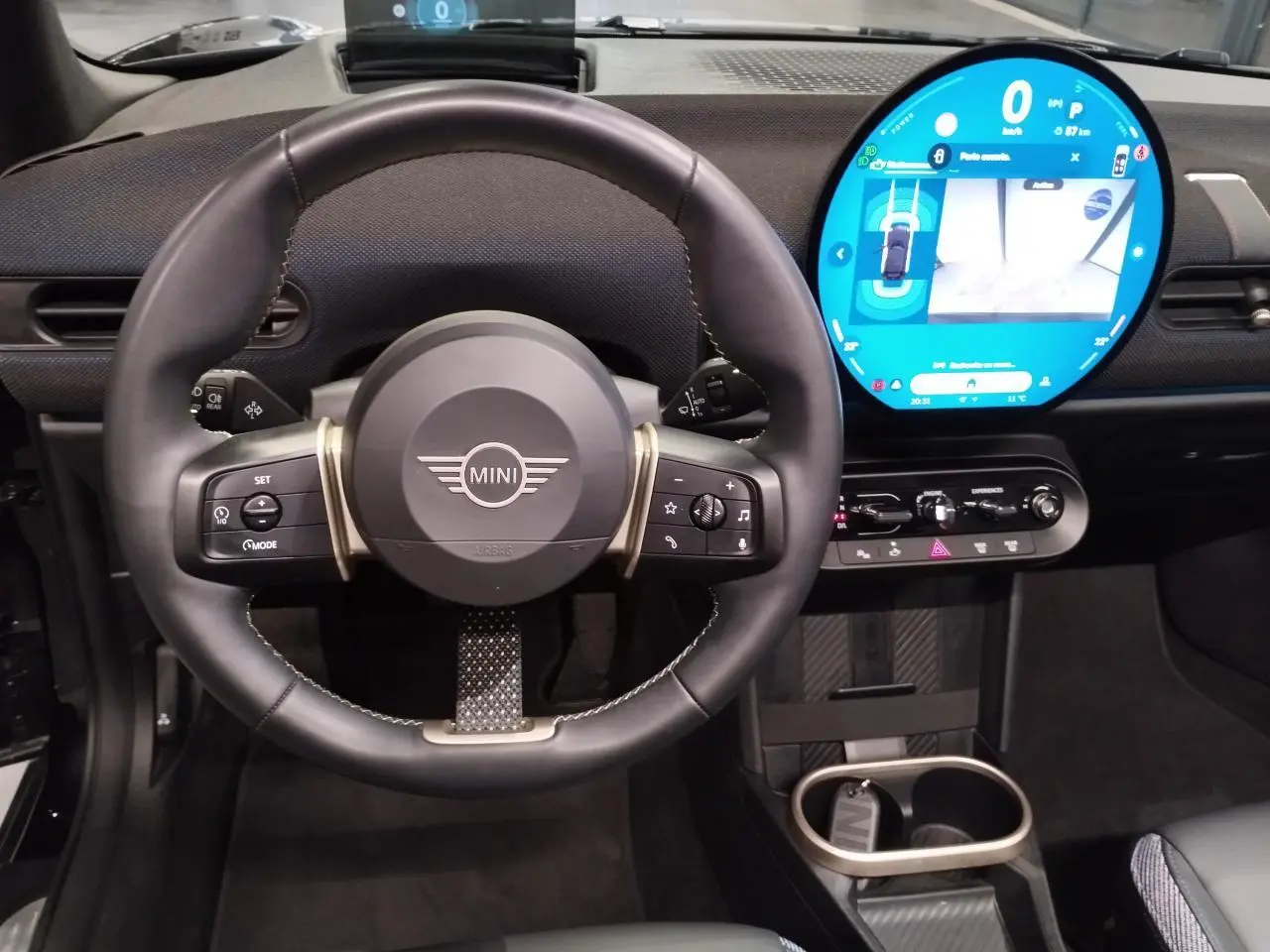 Vue intérieure centrée sur le volant cuir noir et l'écran tactile rond lumineux du tableau de bord MINI Cabriolet 2025.