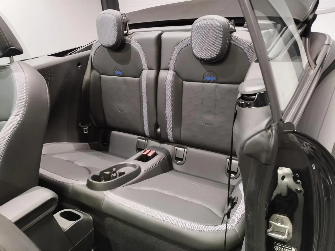 Vue intérieure arrière du cabriolet MINI noir, montrant les sièges arrière en similicuir perforé avec logo MINI brodé.