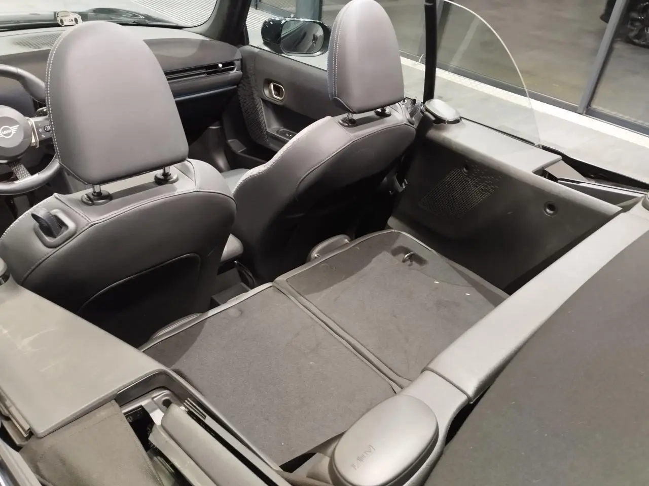 Vue intérieure arrière du cabriolet MINI noir 2025, sièges avant en similicuir perforé noir avec motifs bleus.