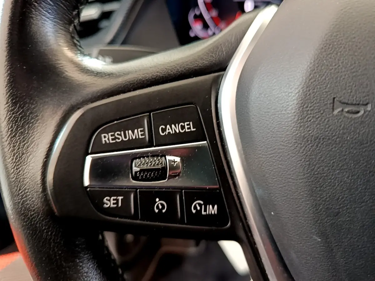 Gros plan sur les commandes de régulateur de vitesse au volant cuir noir d'une BMW Série 1 118i Edition Sport 2023.
