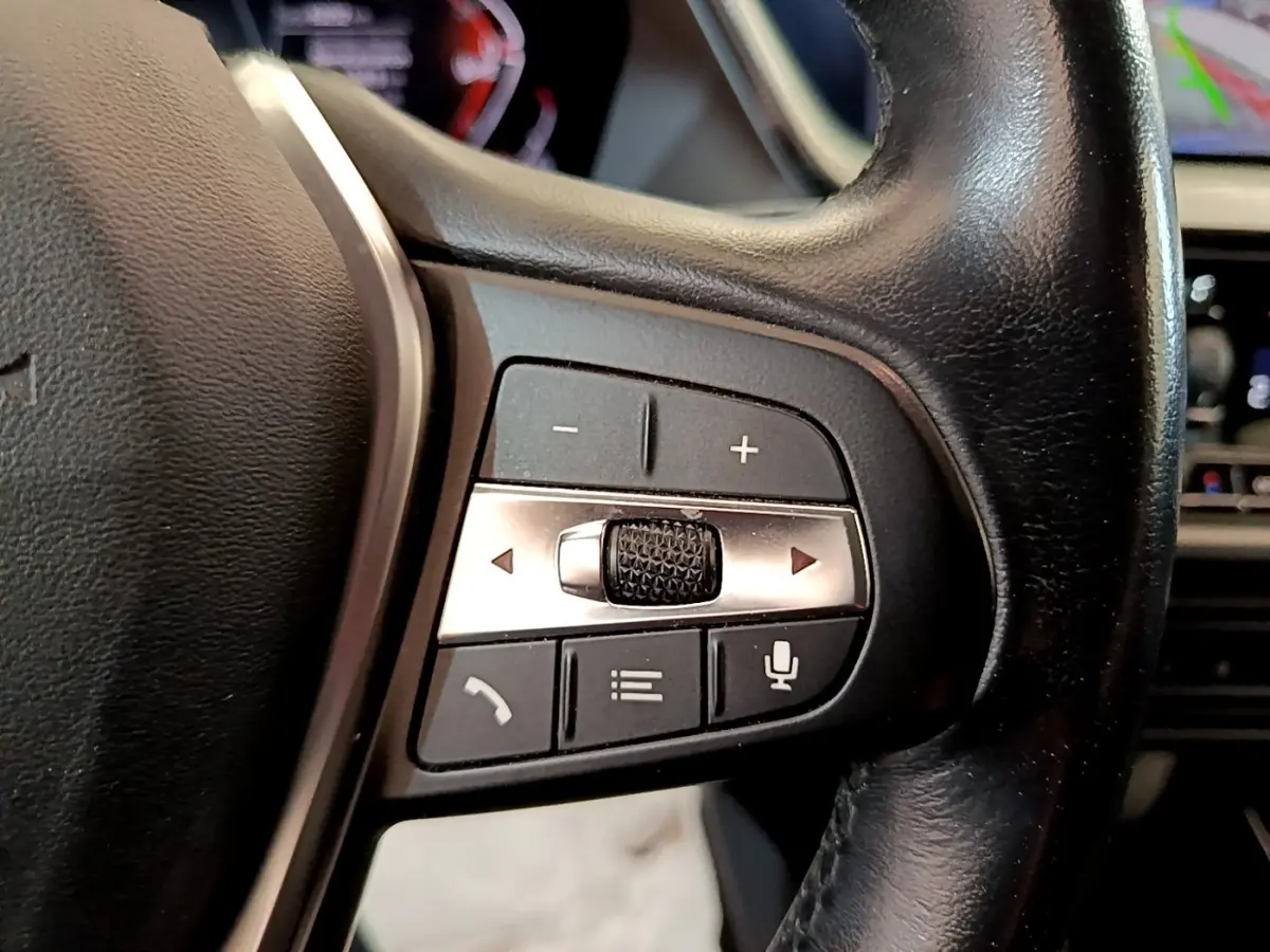 Gros plan sur les commandes du volant côté gauche de la BMW Série 1 118i Edition Sport 2023, cuir noir.