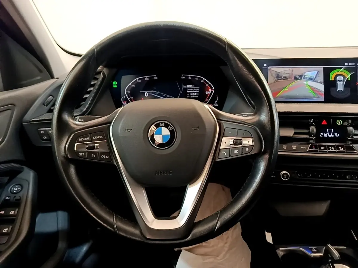 Vue intérieure centrée sur le volant BMW noir et le tableau de bord avec écran tactile affichant la caméra de recul.