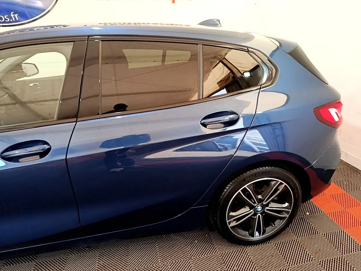 Vue latérale droite sur la partie arrière d’une BMW Série 1 118i Edition Sport bleu avec jante alliage et feux LED allumés.
