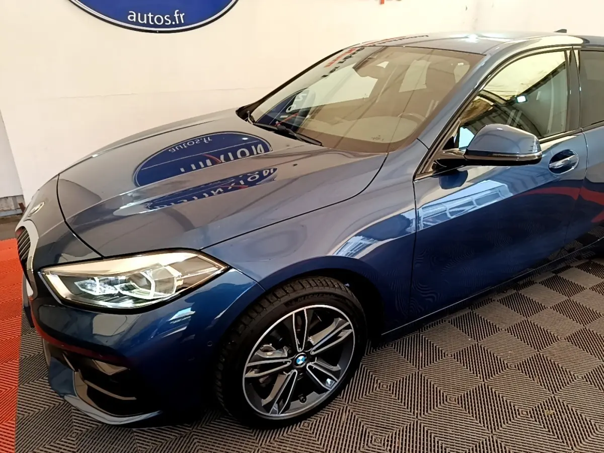 BMW Série 1 118i Edition Sport bleu vue 3/4 avant droit, avec phares LED et jantes alliage distinctives.