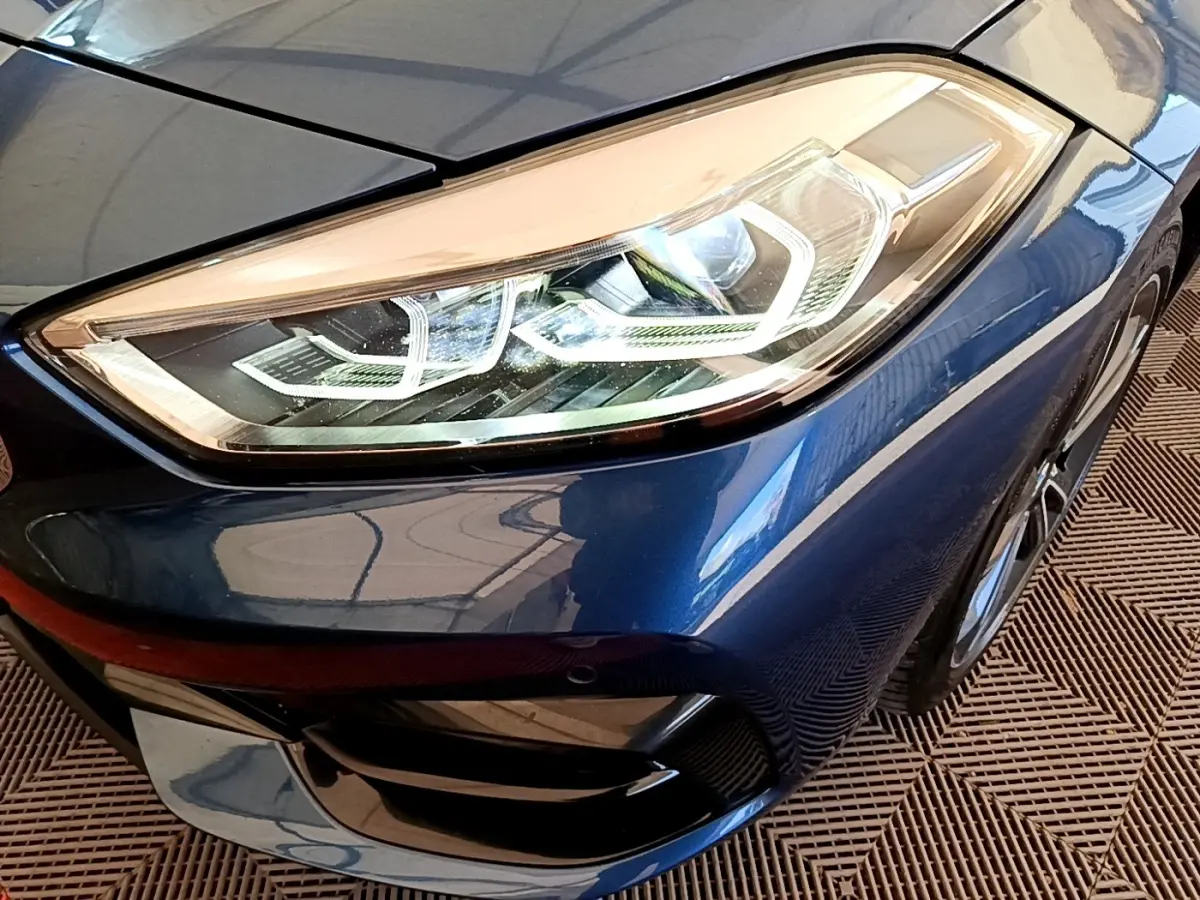 Gros plan sur le phare avant droit bleu d’une BMW Série 1 118i Edition Sport 2023 avec détails LED distinctifs.