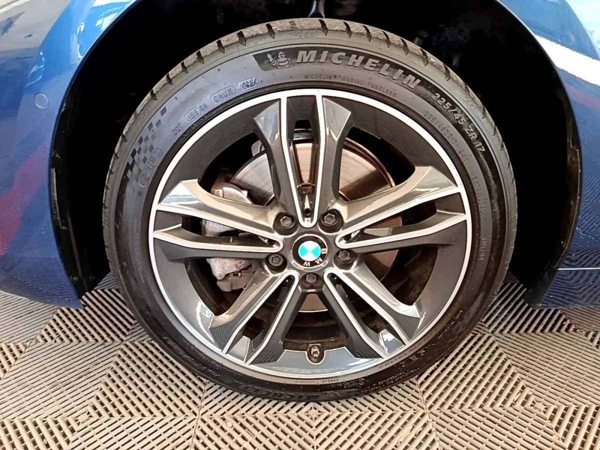 Gros plan sur la roue avant gauche bleu de la BMW Série 1 118i Edition Sport avec jante alliage et pneu Michelin.