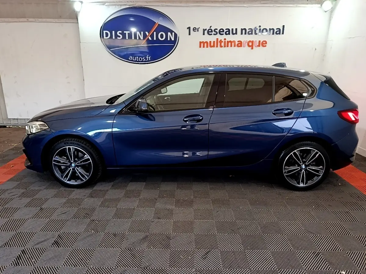 Profil côté gauche d’une BMW Série 1 118i Edition Sport bleu, avec jantes alliage et vitres teintées.