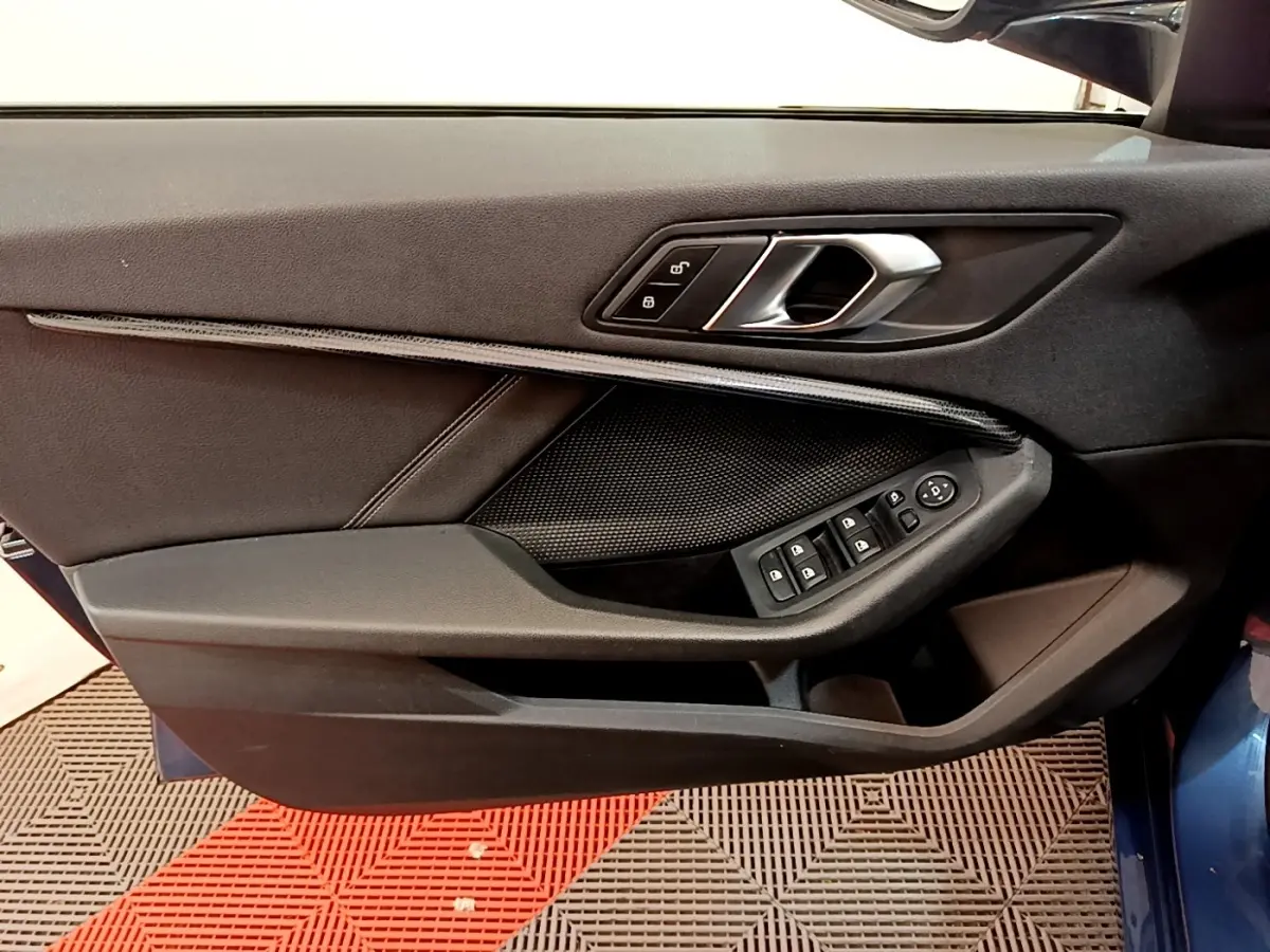 Gros plan sur la porte avant gauche de la BMW Série 1 bleu, montrant la poignée intérieure et les commandes des vitres.