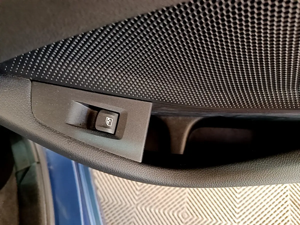 Gros plan sur le bouton de commande de la vitre électrique côté conducteur, avec la porte bleu foncé visible en arrière-plan.