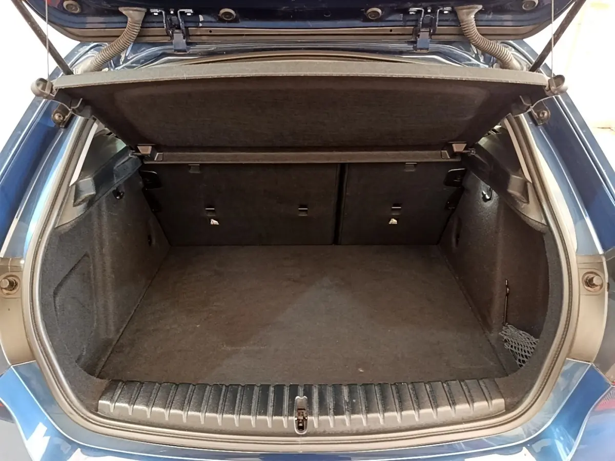 Coffre ouvert vu de l'arrière d'une BMW Série 1 118i bleu, montrant l'espace de chargement vide et la tablette cache-bagages.