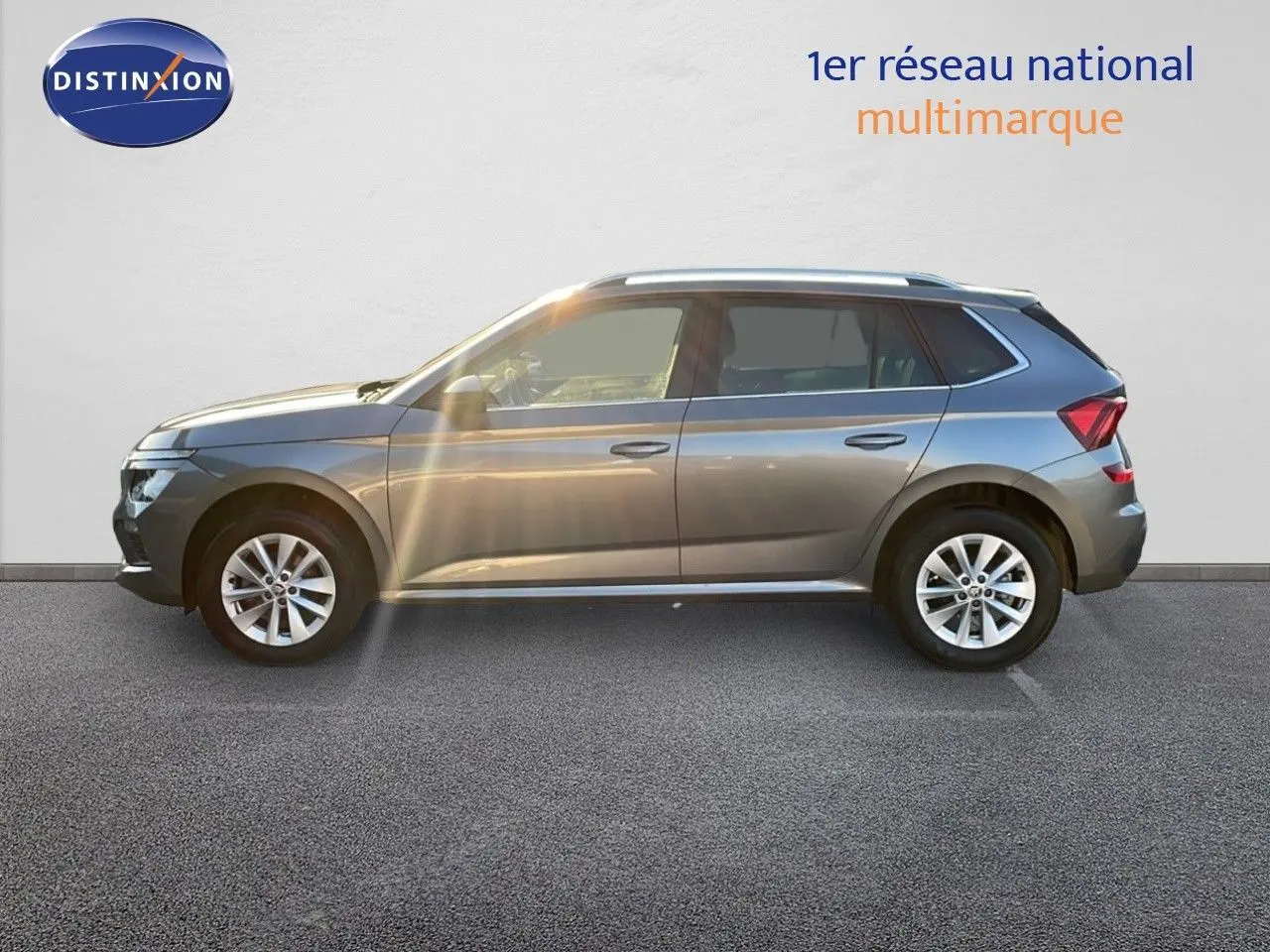 Profil côté gauche d'un Skoda Kamiq gris graphite métallisé 2024 garé devant un mur blanc.