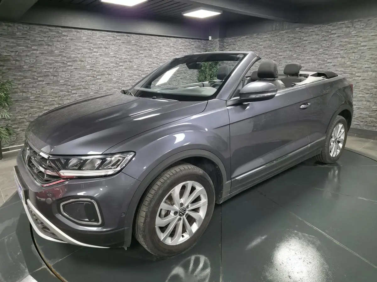Volkswagen T-Roc cabriolet gris métallisé vu de 3/4 avant droit avec capote ouverte en intérieur showroom.