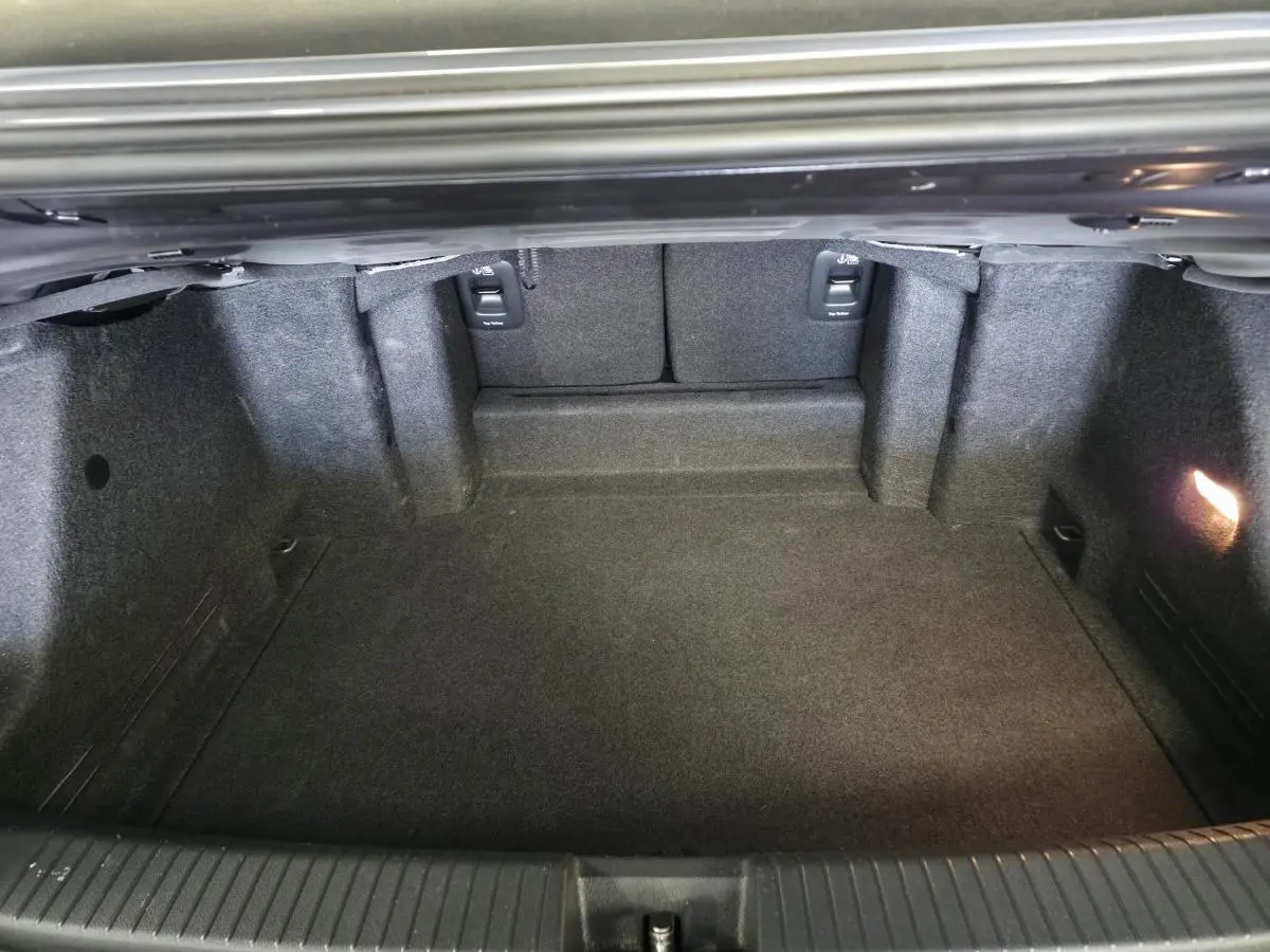 Coffre ouvert vu de l'arrière du Volkswagen T-Roc gris 2024, montrant un espace de chargement propre et éclairé.