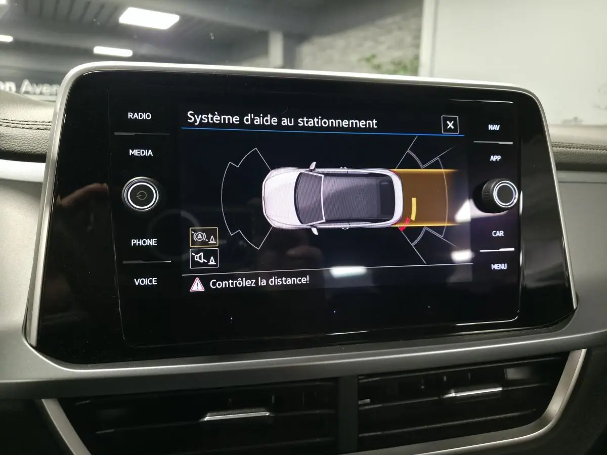 Écran central du Volkswagen T-Roc 2024 affichant l'aide au stationnement avec vue du dessus du véhicule gris.