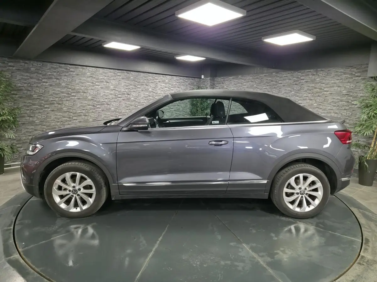 Volkswagen T-Roc Style gris métallisé vue de profil côté gauche avec capote textile noire en intérieur showroom.