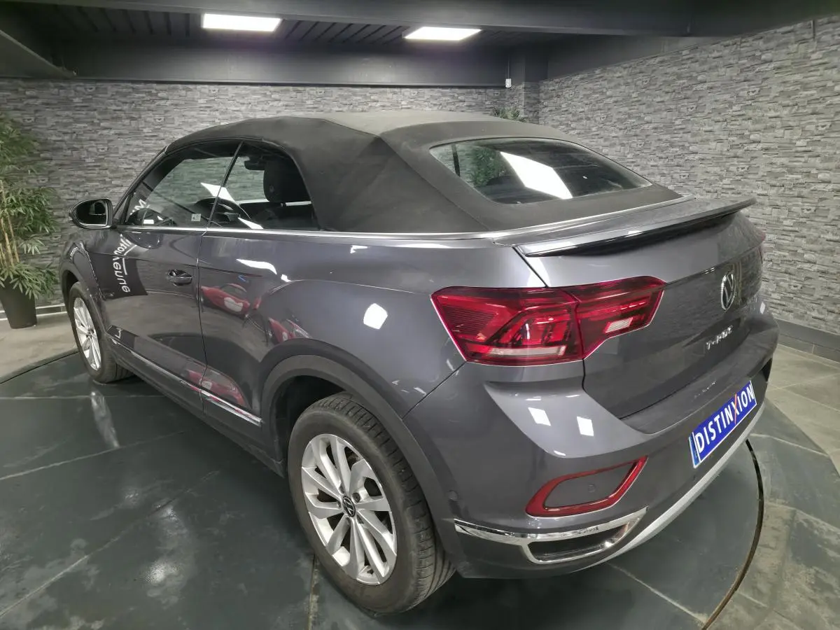 Vue 3/4 arrière droite du Volkswagen T-Roc gris métallisé avec capote noire en intérieur showroom.