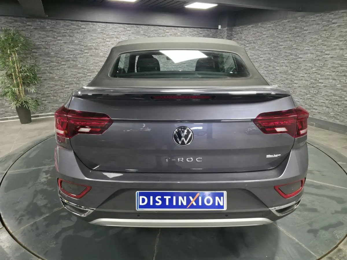 Vue arrière d'un Volkswagen T-Roc gris métallisé avec capote noire en textile dans un showroom.