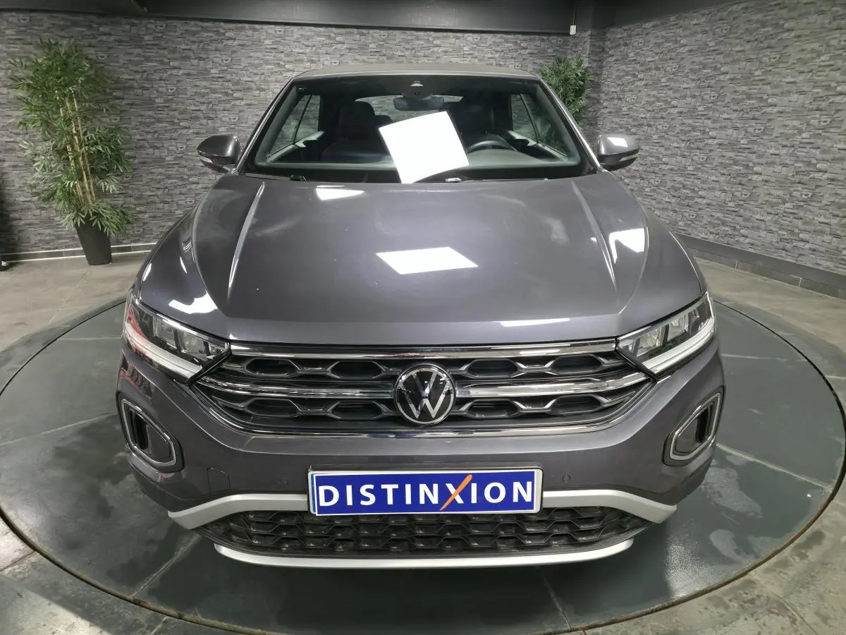 Vue avant d'un Volkswagen T-Roc gris métallisé 2024 avec calandre chromée et logo VW bien visible