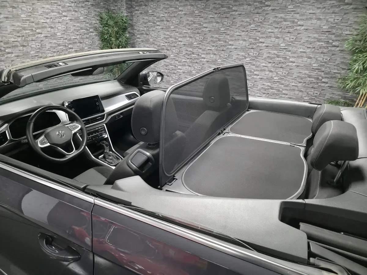 Vue intérieure côté conducteur d'un Volkswagen T-Roc cabriolet gris avec volant multifonction et capote ouverte.