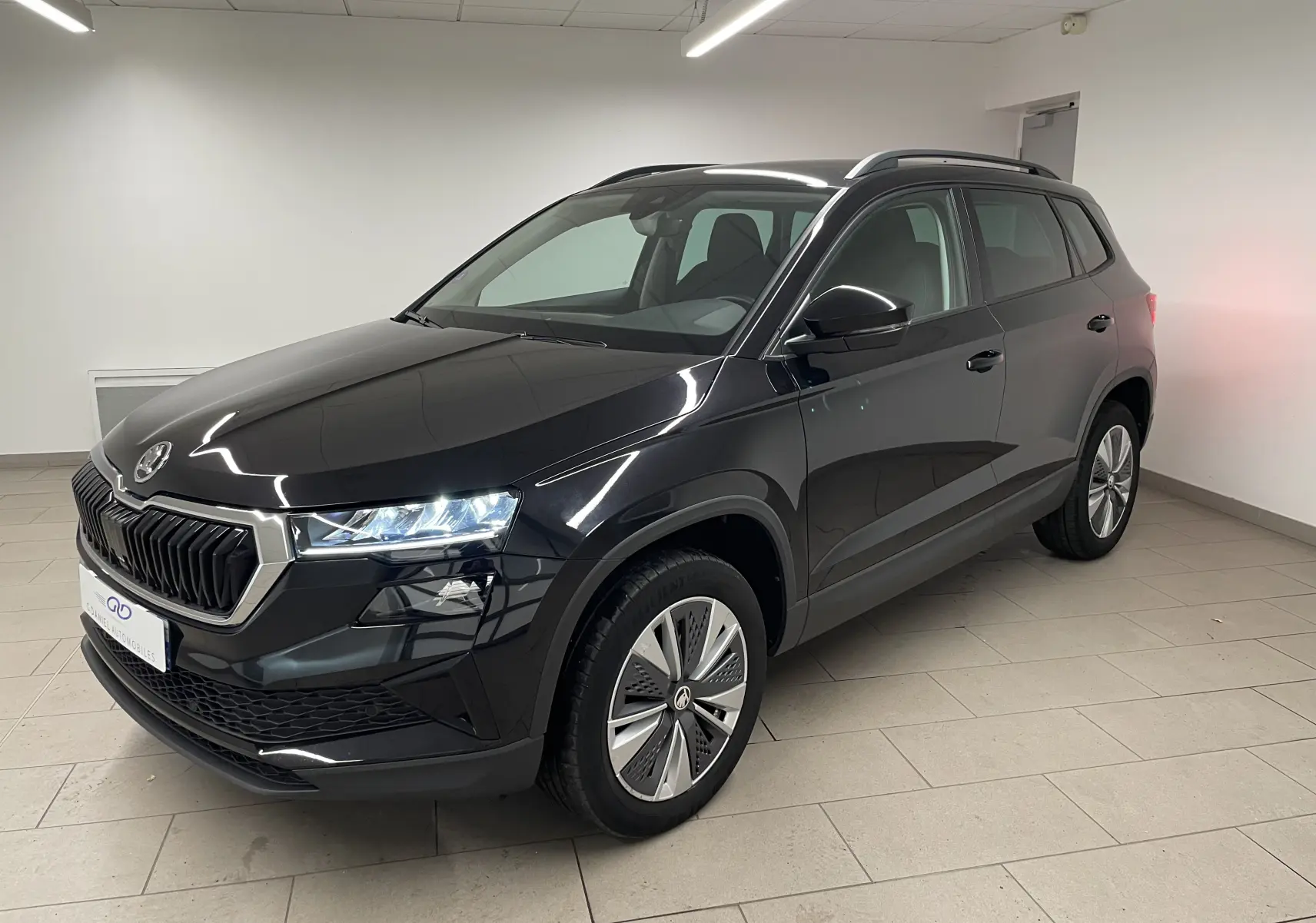 SUV Skoda Karoq noir Magic nacré vu en 3/4 avant droit, avec phares allumés et jantes spécifiques Pack Techno.