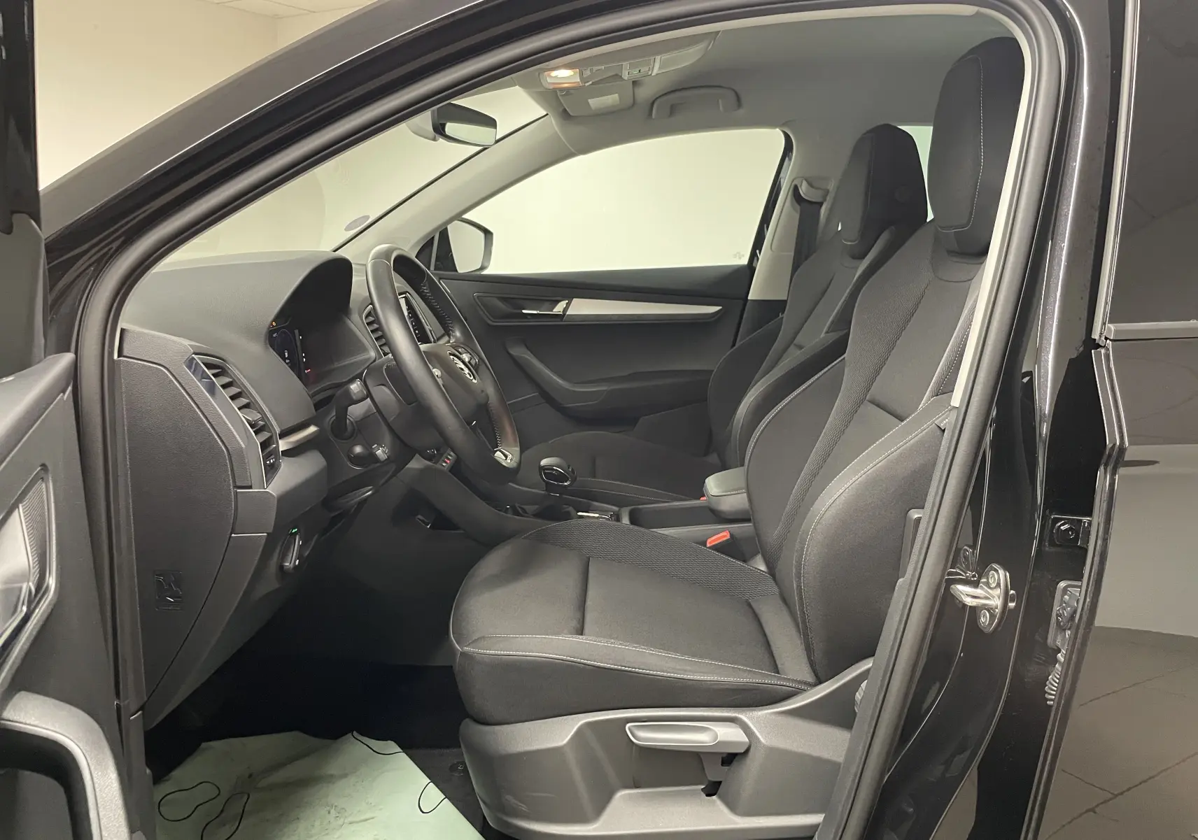 Intérieur côté conducteur du Skoda Karoq noir Magic nacré 2023, sièges tissu et tableau de bord moderne.