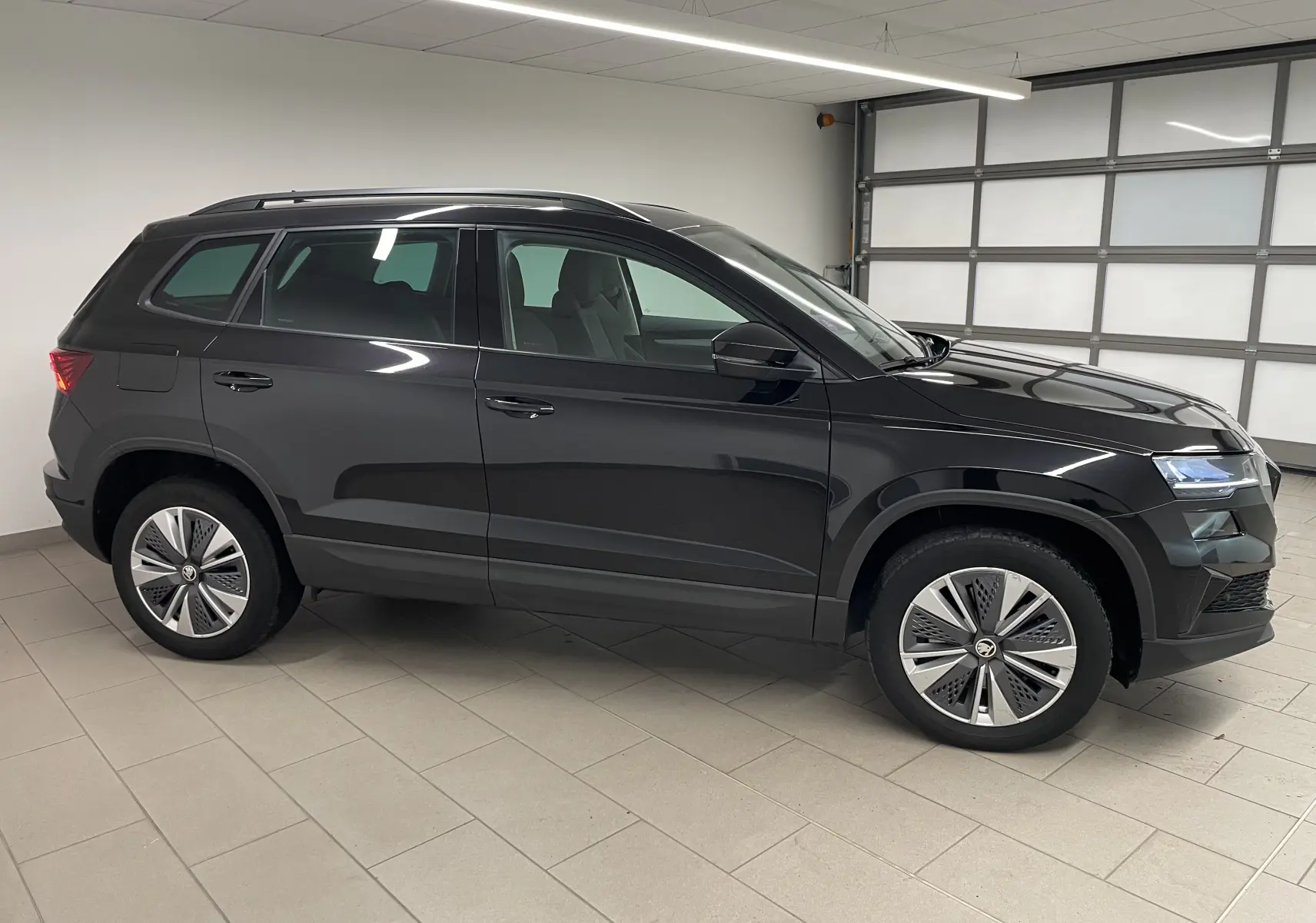 SKODA KAROQ noir Magic nacré vu de profil côté gauche dans un garage, avec jantes modernes et toit noir.