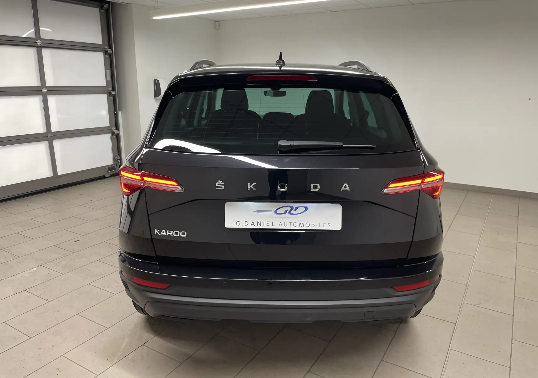 Vue arrière d'un Skoda Karoq noir Magic nacré avec feux allumés dans un garage intérieur.