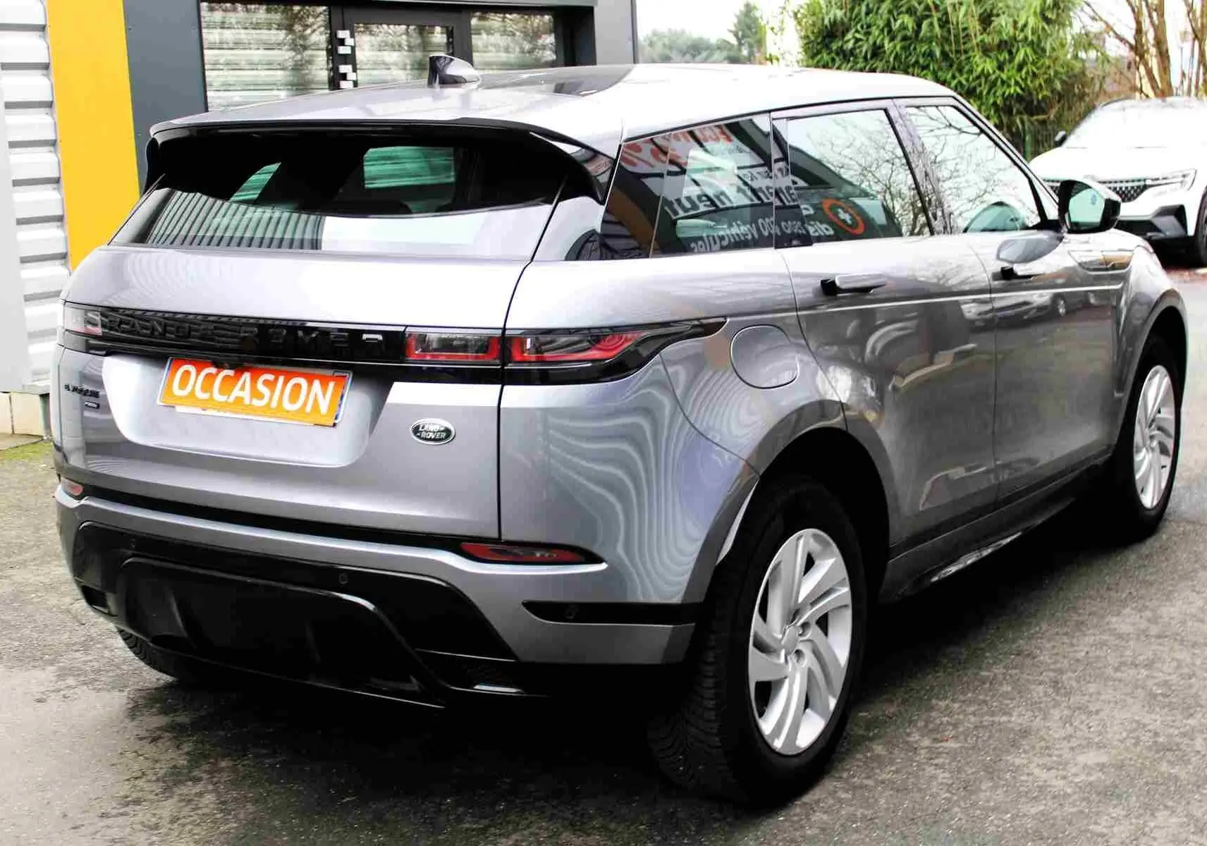 Vue 3/4 arrière droite d'un Range Rover Evoque gris métal 2023 avec badge hybride rechargeable et plaque "OCCASION" visible.