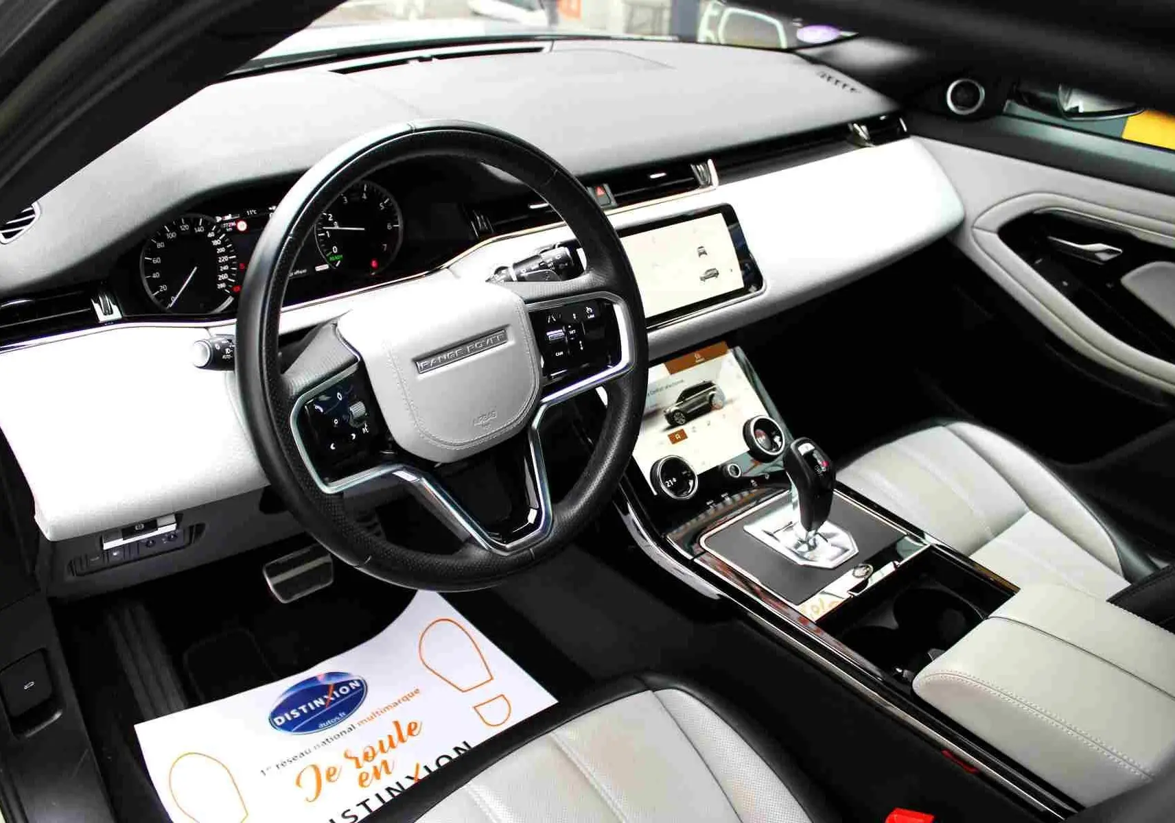 Intérieur clair du Range Rover Evoque 2023, vue côté conducteur, volant multifonction et écran tactile central.